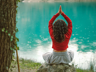 Professora de yoga medita em frente a um lago. Sentimentos nostálgicos frequentemente obscurecem as oportunidades presentes, apesar das dificuldades percebidas