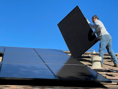 A man stands on a rooftop, securing solar panels one by one 