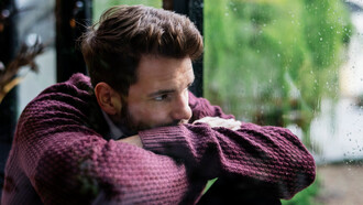 A heartbroken man, looking through the window on a rainy day, waiting for his lover to come back home