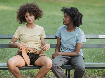 Two curly-haired women sitting on a park bench, talking