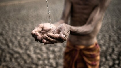 A frail, emaciated man with parched, weathered hands desperately cups a trickle of water against a backdrop of cracked, barren earth—a haunting symbol of extreme drought and deprivation, reflecting the dire consequences of ineffective development aid