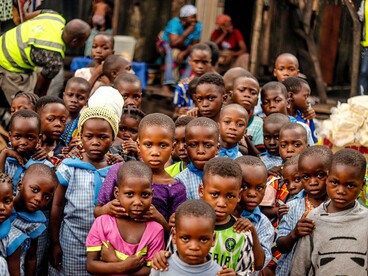 A group of African children pose for a photo, their surroundings reflecting conditions of poverty and malnutrition