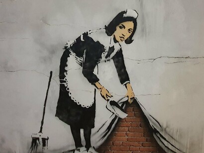 Sweep It Under the Carpet, obra de Banksy, em Londres, Inglaterra. Sobre esta obra, Banksy referiu que "Em tempos idos apenas os Papas e os Príncipes podiam dar-se ao luxo de terem o seu retrato pintado. Aqui temos o retrato de uma empregada chamada Leanne, que limpou o meu quarto de motel em Los Angeles. Ela era uma mulher muito corajosa."