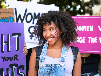 A determined young woman at the forefront of a rally, reflecting the rising voice of women challenging inequality