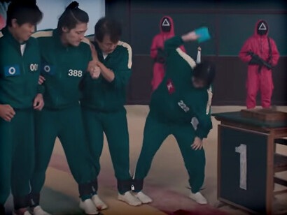 Locked together at the ankles, a player slams red and blue Ddakji tiles onto the ground—every flip a gamble, every slap echoing the price of trust