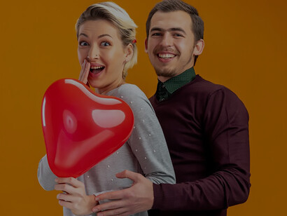 A young couple on Valentine's Day playfully conceals their faces with a heart-shaped balloon, embodying romance and celebration