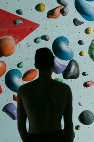 A silhouette of a man standing before a climbing wall, preparing to climb