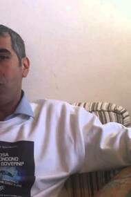 Carlo Di Litta resting comfortably on his sofa wearing a sweater that has an image of the cover of his book  "Cosa Nascondono I Nostri Governi?"