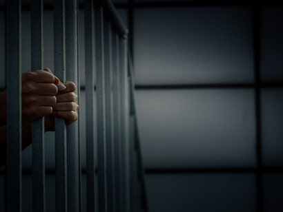 Hands of man on a bar, locked up in jail