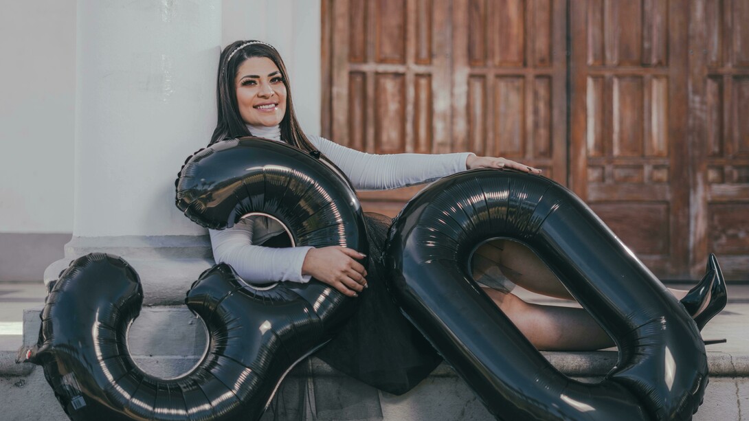 A woman sitting on the floor with balloons, celebrating her 30th birthday