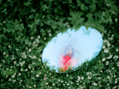 Staring into the mirror on the ground, she contemplates the importance of embracing raw, unfiltered emotions in a culture often dominated by irony and detachment