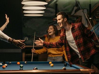 Several young adults sharing laughter over a pool game, illustrating the quiet rebellion of choosing presence over productivity