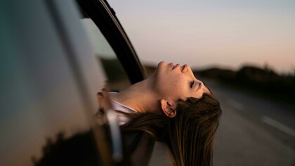 A woman leans out of a car window, enjoying the fresh air
