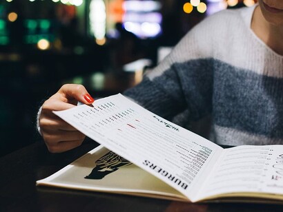 Close-up of hands holding a menu at a busy restaurant, struggling to choose from too many food options