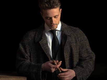 A man wearing a tweed coat is lighting his cigar