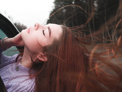A car window frames a woman with vibrant red hair leaning out gracefully