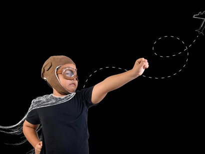A boy, embodying a superhero, plays exuberantly in front of a black wall adorned with white drawings, showcasing his creativity and imagination