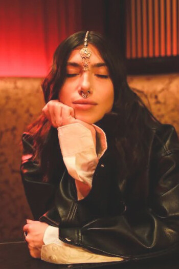 A stylish Indian woman in a leather jacket, with a septum piercing and maang tikka, looking thoughtfully into the distance