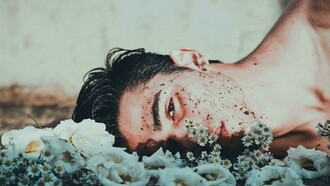 A man lies down next to daisies, looking upset
