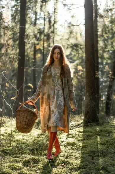 A young woman with long red hair, dressed in linen, walks alone through the forest gathering mushrooms
