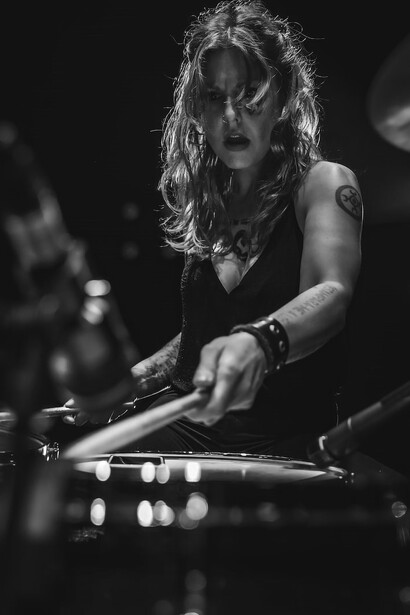 A woman, clad in a black long-sleeve shirt, skillfully pounding the drums