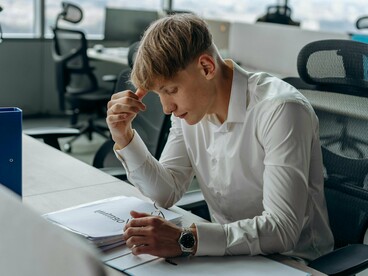 Jovem com olhar cansado e postura tensa no ambiente corporativo. A frustração de perceber que o mercado exige competências que não foram desenvolvidas