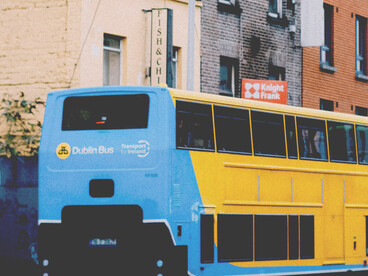 A blue-and-yellow old double-decker bus driving along a rain-wet cobblestone street in Dublin, Ireland