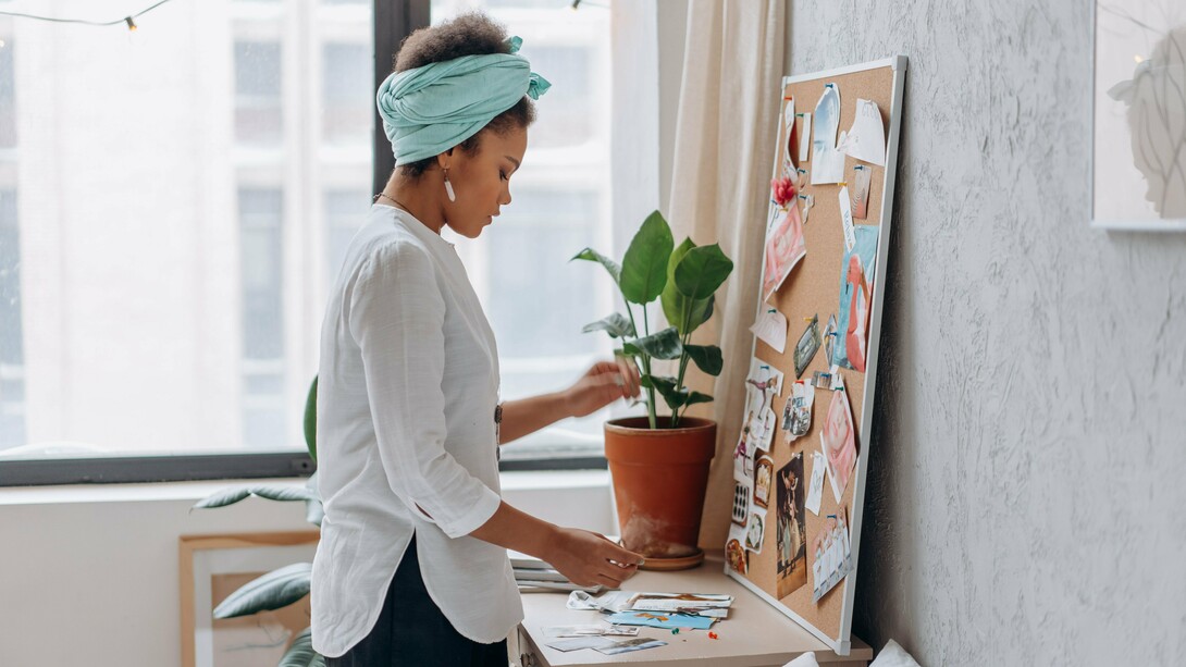 A woman arranging images and ideas on a vision board, representing the process of designing a self-care routine around personal needs and desires