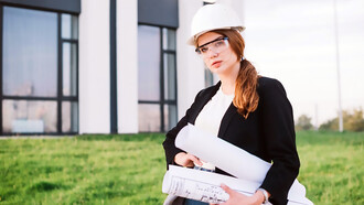 A female architect stands confidently in front of a building, holding architectural plans in her hands