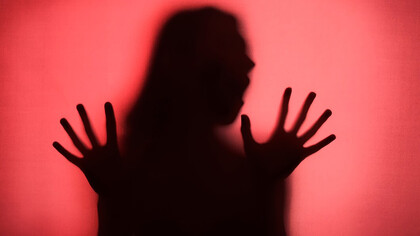 A silhouette of a woman stands gracefully behind flowing red curtains