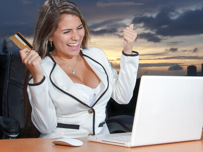 With a smile, the woman confidently shops online, holding a credit card, enjoying the convenience of e-commerce