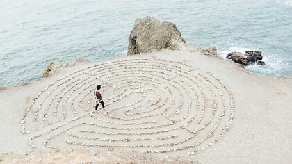 Amidst the healing embrace of a labyrinth, a person walks along the sunlit beach, unveiling the secrets of the universe with each step, as the tranquil expanse offers solace and revelations