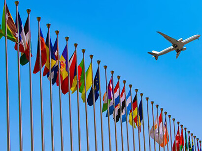 A tapestry of flags adorns the United Nations headquarters, gently swaying in the breeze, while overhead, a plane glides through the sky, adding a dynamic touch to the diplomatic tableau