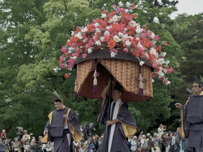 La festividad evoca una estampa de tradición y gracia en la que la protagonista destaca como una «malva rutilante», concepto estrechamente vinculado al propio simbolismo botánico del Aoi Matsuri (el festival de la malva real)