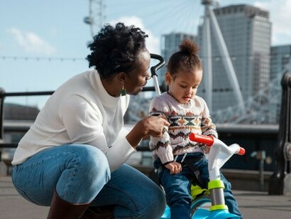 A woman and her child ride a tricycle together in the park