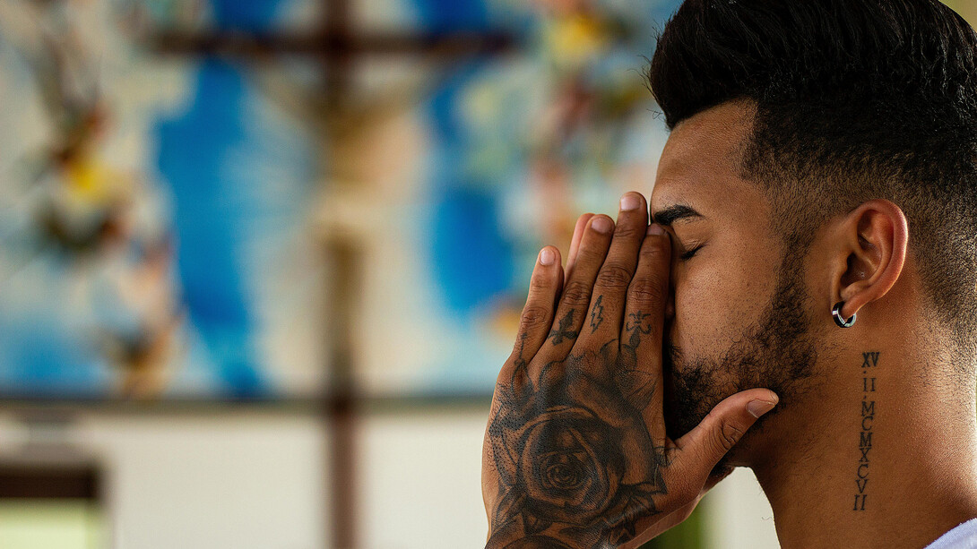 A man with closed eyes, holding his face in both hands, praying in church, seeking peace and spiritual renewal in the midst of his struggle