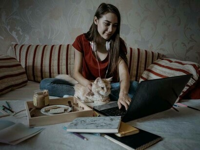 A young employee working from home on her laptop with her cat