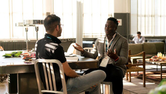 Two men engage in a deep conversation, pondering the complexities of merit and achievement, as they navigate the challenges of imposter syndrome and the deserving threshold