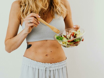 A toned woman eats a vegetable salad while working toward healthy weight loss