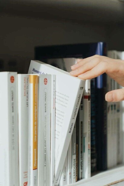 Mano che seleziona un libro di Balzac da uno scaffale ordinato, pieno di classici della letteratura francese e russa