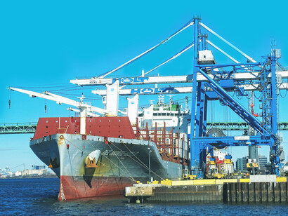 A cargo ship sails on the sea under a clear blue sky during the day, heading towards the bustling harbor in China