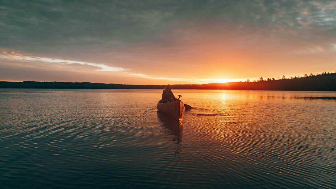 A woman drifting through Ely Lake, Minnesota beneath the fading Minnesota sky, reflecting the deep connection between nature, solitude, and healing
