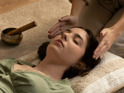 A woman lies still in deep relaxation as healing hands press gently on her forehead