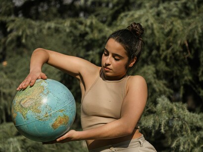 Uma mulher sustenta um globo terrestre em meio às árvores, compondo uma imagem que simboliza a união entre humanidade e planeta. Gaia representa a Terra como organismo vivo e interdependente