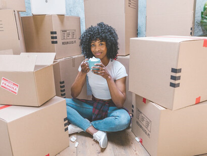 Amidst an array of cardboard boxes, a woman sits in reflection holding a cup, symbolizing her impending move to a new place