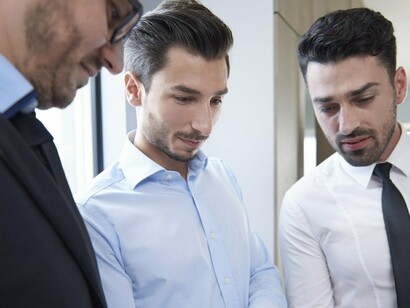 Three businessmen huddled around a computer, analyzing data to better serve their interests