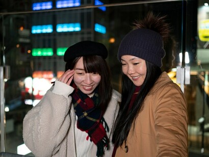 Two joyful young women laughs and chats while hanging out in the lively streets of South Korea's urban scene