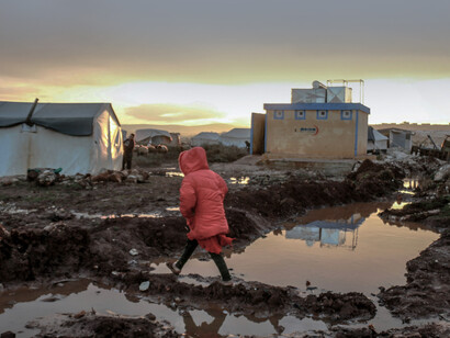 In Idlib, Idlib Governorate, Syria, people gather around rows of tents in a refugee camp, set against muddy and challenging conditions