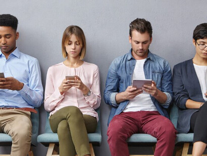 A group of people in a waiting room stare silently at their phones