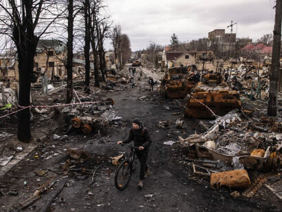 Un hombre empuja su bicicleta entre escombros y vehículos militares rusos destruidos en Bucha, 2022, noroeste de Kiev, Ucrania